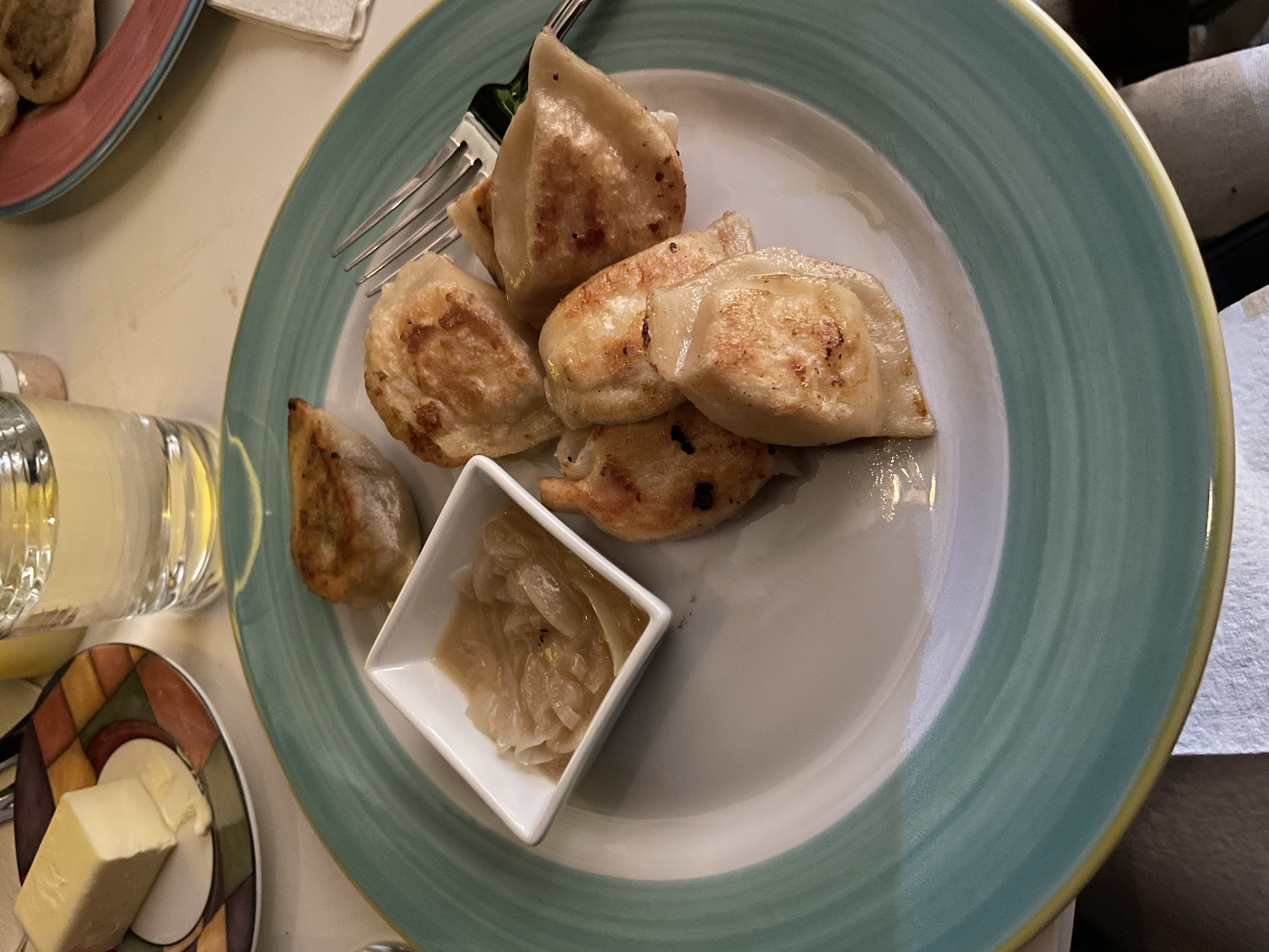 plate of pierogi on a green plate with a cup of water and a dish of onion